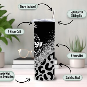 May include: A stainless steel tumbler with a black background and a silver glitter design. The tumbler has a leopard print pattern at the bottom and the words "be kind" in a circular design. It includes a straw and a splashproof sliding lid.