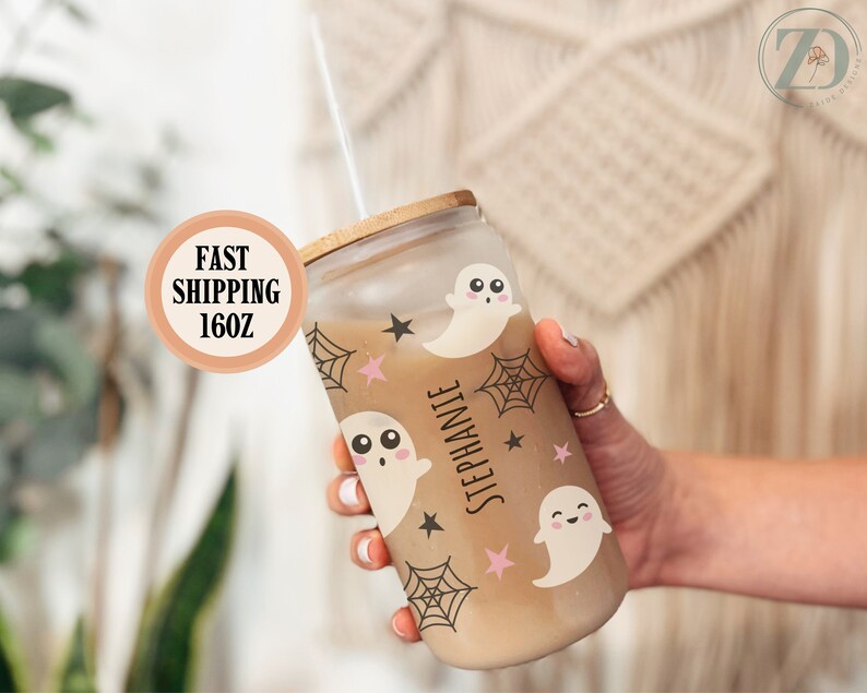 May include: A clear glass tumbler with a bamboo lid, filled with a beverage and a straw. The tumbler is decorated with cute ghost and spiderweb graphics. The name "Stephanie" is printed vertically on the side. The tumbler holds 16 ounces.