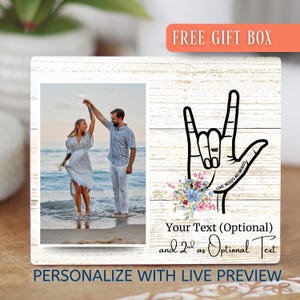 May include: A white wooden picture frame with a photo of a couple dancing on a beach. The frame features a black hand gesture with the text "LOVE NEEDS NO WORDS" and a floral arrangement. The frame includes the text "Your Text (Optional)" and "PERSONALIZE WITH LIVE PREVIEW".