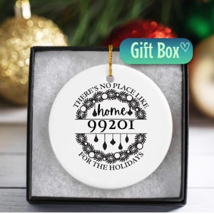 May include: A white ceramic holiday ornament with the text "THERE'S NO PLACE LIKE HOME FOR THE HOLIDAYS" and the zip code 99201. The ornament is in a black gift box with a gold string for hanging.