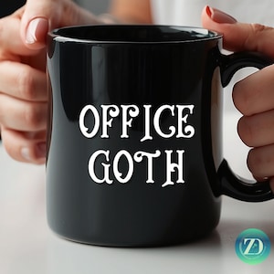 May include: Black ceramic mug with the white text "OFFICE GOTH". The mug has a curved handle and is held by a person. The mug is a standard size for coffee or tea.