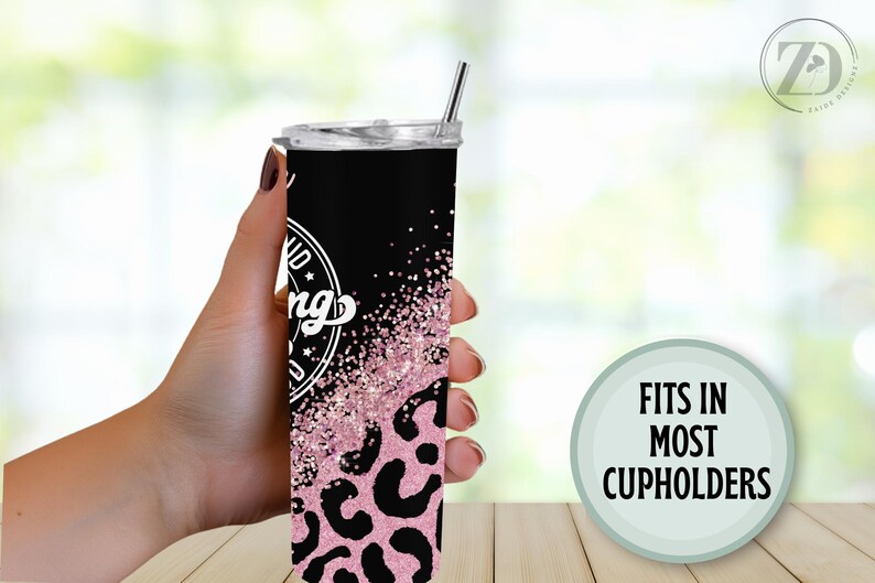 May include: A black and pink tumbler with a leopard print design and the words "Kind of a big deal" in a white circle. The tumbler has a silver straw and the text "Fits in most cupholders" in a green circle.