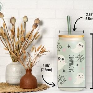 May include: A personalized 5.9-inch (15cm) tall glass tumbler with a bamboo lid and a green straw. The tumbler features a light green background with ghost and spiderweb designs. The name "STEPHANIE" is printed vertically on the tumbler.