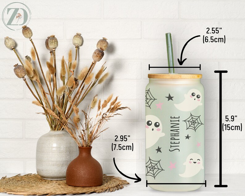 May include: A personalized 5.9-inch (15cm) tall glass tumbler with a bamboo lid and a green straw. The tumbler features a light green background with ghost and spiderweb designs. The name "STEPHANIE" is printed vertically on the tumbler.