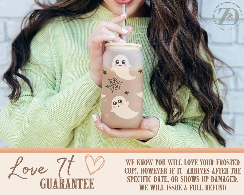 May include: Frosted glass cup with a bamboo lid and straw, decorated with cute cartoon ghosts, spiderwebs, and stars. The cup is held by a person wearing a light green sweater. The cup has the text "Love It Guarantee".