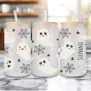 May include: Three frosted glass beverage cups with wooden lids and straws. The cups feature a repeating pattern of smiling ghosts, spiderwebs, and stars in black and pink. One cup is personalized with the name "Stephanie".