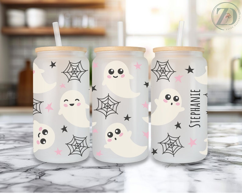 May include: Three frosted glass beverage cups with wooden lids and straws. The cups feature a repeating pattern of smiling ghosts, spiderwebs, and stars in black and pink. One cup is personalized with the name "Stephanie".