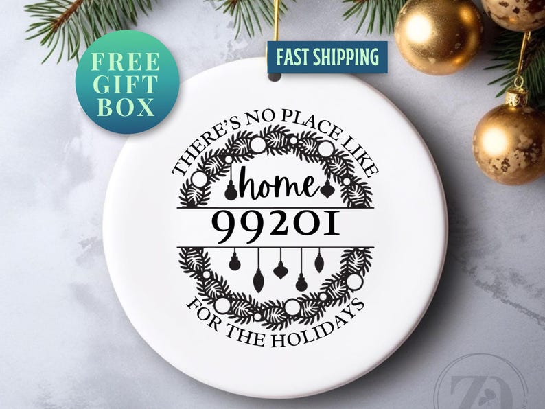 May include: White ceramic Christmas ornament with the text "There's no place like home for the holidays" and the zip code 99201. The design includes a wreath and hanging ornaments. A "Free Gift Box" sticker is visible.