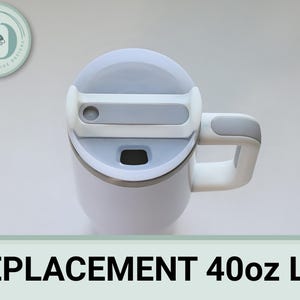 May include: White 40oz tumbler with a gray lid and handle. The lid has a sliding closure and a small opening. The handle is curved and attached to the side of the tumbler. The text "REPLACEMENT 40oz LID" is at the bottom.