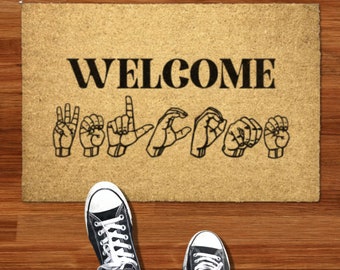May include: A brown doormat with the word "WELCOME" in black letters. The word is spelled out in American Sign Language.