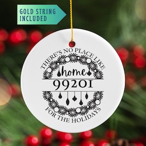 May include: A white ceramic holiday ornament with the text "THERE'S NO PLACE LIKE home FOR THE HOLIDAYS" and the zip code 99201. The design includes a wreath and hanging ornaments. A gold string is attached for hanging.