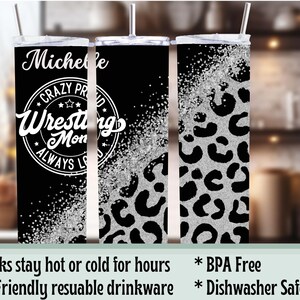 May include: A black and silver tumbler with a lid and straw. The tumbler features the name "Michelle" and the text "Crazy Proud Wrestling Mom Always Loves" in white. The right side has a silver leopard print.