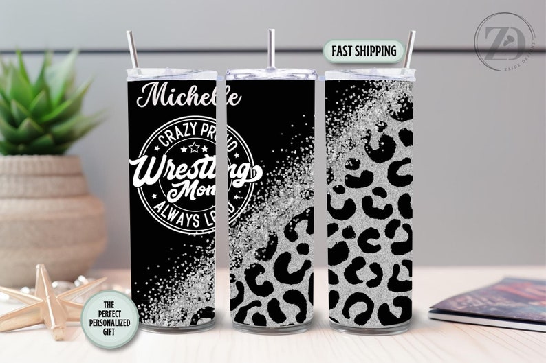 May include: A personalised tumbler with a black background and silver glitter accents. The tumbler features the text "Michelle" and "Crazy Proud Wrestling Mom" in white. The design includes a leopard print pattern.