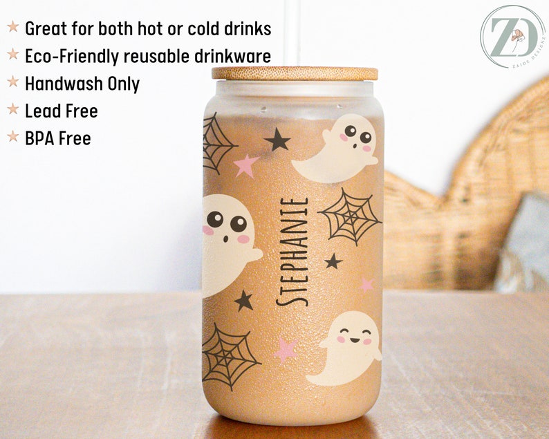 May include: A glass tumbler with a bamboo lid, decorated with cartoon ghosts, spiderwebs, and stars. The name "STEPHANIE" is printed vertically on the tumbler. The tumbler is designed for both hot and cold drinks.