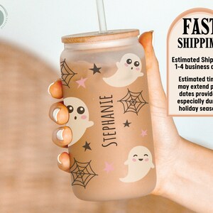 May include: A frosted glass can-shaped tumbler with a bamboo lid, straw, and a Halloween theme. The design includes cartoon ghosts, spiderwebs, and stars in brown and pink. The name "STEPHANIE" is printed vertically on the glass.