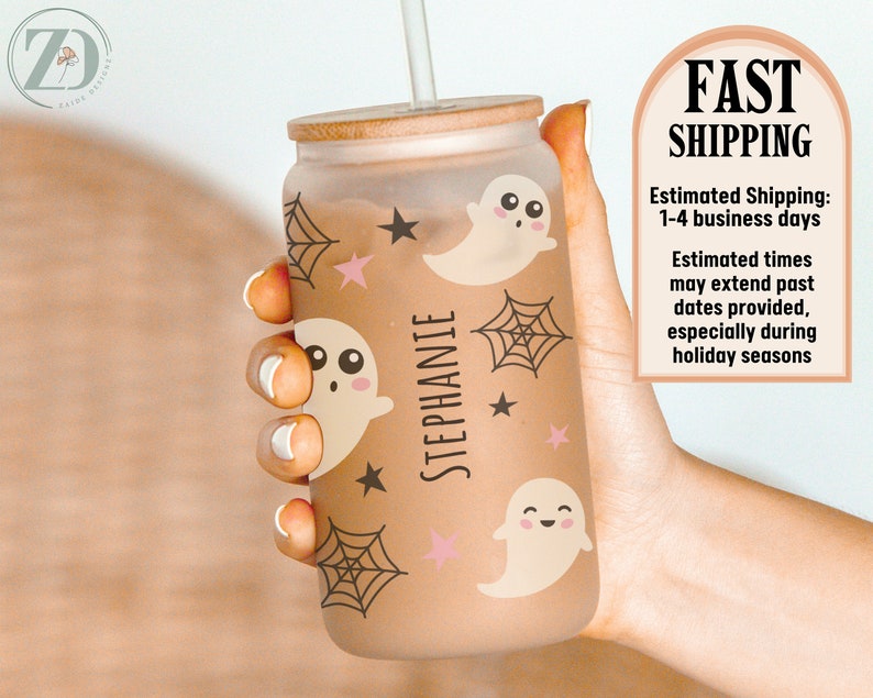 May include: A frosted glass can-shaped tumbler with a bamboo lid, straw, and a Halloween theme. The design includes cartoon ghosts, spiderwebs, and stars in brown and pink. The name "STEPHANIE" is printed vertically on the glass.