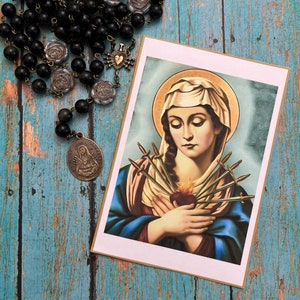 May include: A religious print featuring a painting of the Virgin Mary with seven swords piercing her heart. The image is set against a blue and green background.