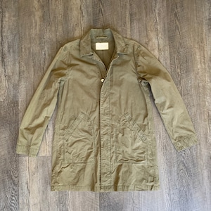 May include: A long-sleeved, olive green utility jacket with a button closure and two large pockets on the front.