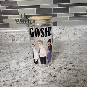 May include: A clear glass tumbler with a bamboo lid, featuring the word "GOSH!" in bold black letters. The tumbler has a graphic of three men. The Witch's Craft Room logo is visible on the left side.