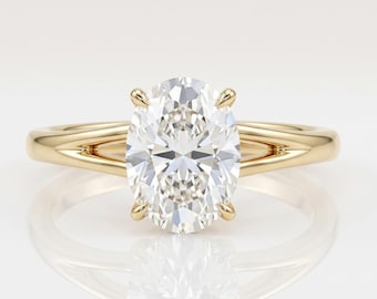May include: A gold ring featuring a large, oval-cut, clear gemstone set in a four-prong mounting. The band is crafted from polished yellow gold and splits into two distinct, slender arms as it reaches the central stone, creating a sleek design.