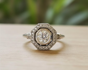 Könnte beinhalten: Ein silberner Verlobungsring mit einem großen, runden, klaren Diamanten im Zentrum. Der Mittelstein ist von einem Halo aus kleineren Diamanten in achteckiger Form umgeben. Zusätzliche kleine Diamanten sind auf dem Ringband gesetzt.