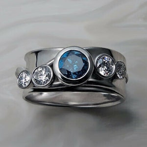 May include: A silver ring with a blue gemstone and three smaller white gemstones. The ring is made of two bands, one wider than the other.