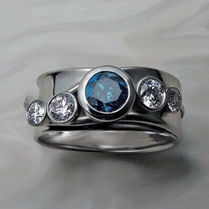 May include: A silver ring with a blue gemstone surrounded by smaller white gemstones. The ring has a unique design with a curved band.