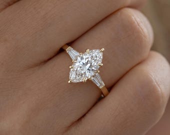 May include: A gold ring featuring a large marquise-cut center diamond held by six prongs, flanked by two smaller baguette-cut diamonds on each side. The band is crafted from polished yellow gold, creating a classic and elegant appearance.