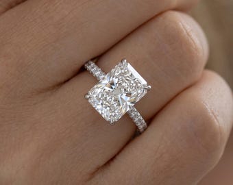 May include: A silver-toned ring featuring a large, rectangular radiant-cut center stone held by four prongs. The slender band is adorned with a series of small, round-cut pavé diamonds extending along the sides of the metal shank.
