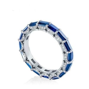 May include: A silver ring featuring a band of rectangular, deep blue gemstones. The ring is embellished with small, clear gemstones between the blue stones. The ring is set against a white background.
