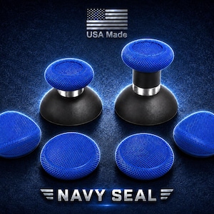 Puede incluir: Un conjunto de joysticks para mando en azul y negro con superficies texturizadas para mayor agarre. Incluye dos sticks altos con anillos plateados y cuatro tapas bajas. El texto USA Made y NAVY SEAL es visible sobre el fondo azul oscuro.