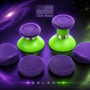 May include: A set of purple and lime green controller thumbsticks featuring textured circular tops. Two thumbsticks are mounted on lime green bases, while four additional purple textured caps are arranged below. The text USA Made and GALAXY appear.