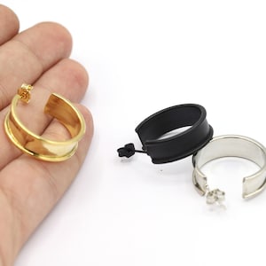 Könnte beinhalten: Drei Paar Creolen in Gold, Schwarz und Silber. Die Ohrringe sind alle gleich groß und in der gleichen Form, aber sie haben unterschiedliche Farben.