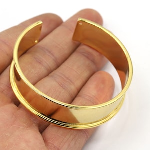 Peut inclure: Un bracelet jonc en métal doré avec une surface lisse et arrondie. Le bracelet est ouvert d'un côté et présente une légère courbure.