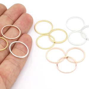 Puede incluir: Surtido de anillas de salto de metal en oro, plata y oro rosa. Las anillas son de diferentes tamaños y están dispuestas en una pila sobre una superficie blanca.