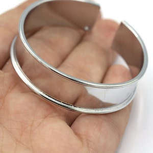 May include: A silver metal bangle bracelet with a wide, flat band. The bracelet has a smooth, polished finish.