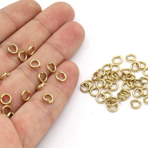Könnte beinhalten: Ein Haufen goldener Sprungringe, eine Art Schmuckzubehör, liegt auf einer weißen Oberfläche verstreut. Einige Sprungringe werden in einer Hand gehalten.