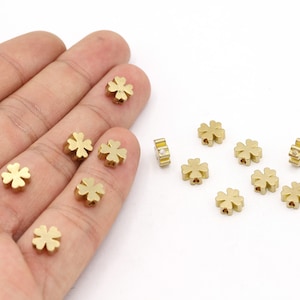 May include: A collection of gold-colored metal four-leaf clover charms. The charms are small and have a delicate design.