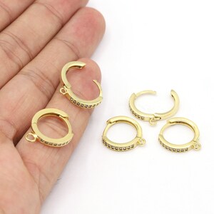 May include: Four gold-toned hoop earring findings with a small loop at the bottom. Each hoop is decorated with a row of clear sparkling stones.