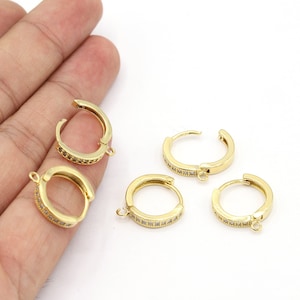 May include: Five gold hoop earrings with a clear crystal embellishment around the edge. Each earring has a jump ring for attaching a charm or pendant.