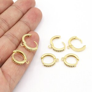 May include: Five gold hoop earrings with clear rhinestones. The hoops are open and have a hinged closure.