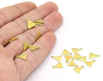 May include: A group of gold triangle-shaped metal charms with a jump ring at the top. The charms are scattered on a white surface.