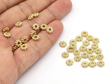May include: A pile of gold-colored metal beads with a flower-shaped design. The beads are small and have a hole in the center.