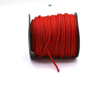 May include: A spool of red cord wound around a black plastic bobbin.