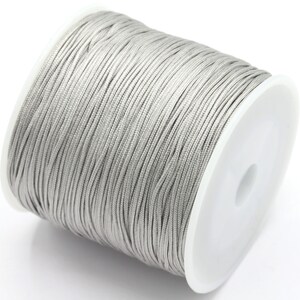 May include: A spool of silver gray waxed cord. The cord is wound tightly around a white plastic spool.