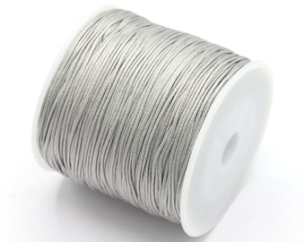 May include: A spool of silver gray waxed cord. The cord is wound tightly around a white plastic spool.