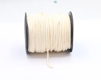 Può includere: Una bobina di corda bianco sporco. La corda è avvolta attorno a una bobina di plastica nera. La corda sembra essere fatta di un materiale ritorto e strutturato. Lo sfondo è bianco.
