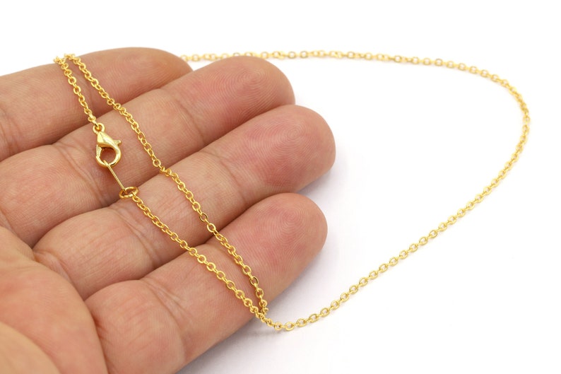 May include: A gold chain necklace with a lobster clasp closure. The chain is delicate and has a fine, round link design.