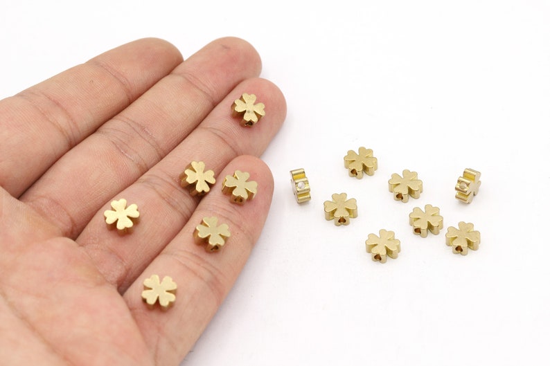 May include: A collection of gold-colored metal four-leaf clover charms. The charms are small and have a delicate design.