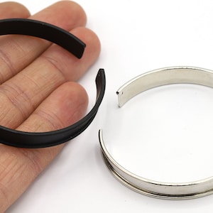 Op de afbeelding: Twee metalen armbandjes, een zwart en een zilveren. Beide armbandjes zijn rond en hebben een simpel ontwerp.